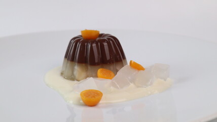 chocolate coconut pudding on a white plate with small orange fruit topping