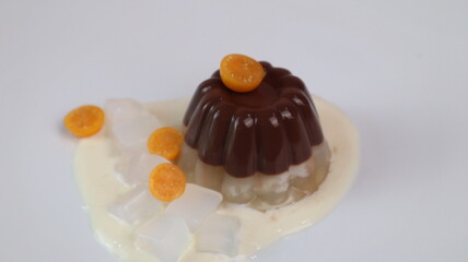 chocolate coconut pudding on a white plate with small orange fruit topping