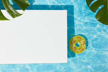 Minimal poolside scene with white platform, tropical leaves, and inflatable ring floating on clear...