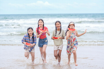 group of multiracial friends holding watermelon,enjoying on the beach,children running together in...