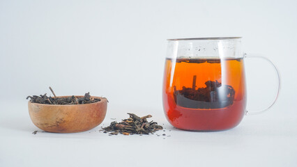 Tea in a glass teapot with a bowl of ground tea leaves isolated on white background