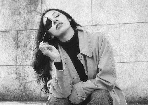 Fashion model posing with sunglasses and trench coat in black and white