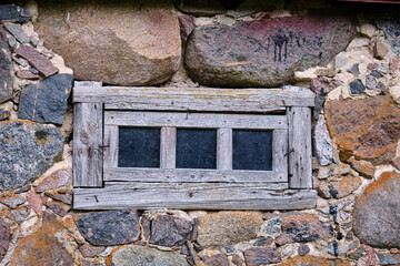 Rustic wooden window framed by an ancient stone wall in a historic building during overcast weather