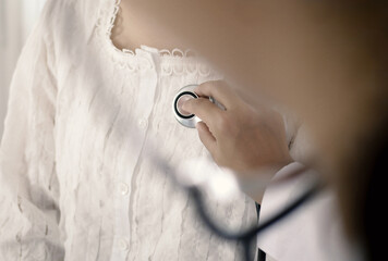 A caring and sensitive doctor is using a stethoscope to listen to the patient's heart and lungs, in...