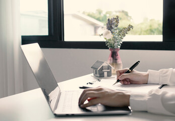 A young woman real estate service worker is sitting at a computer searching for information and...
