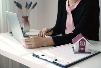 A young woman real estate service worker is sitting at a computer searching for information and arranging house rentals for clients with care and professionalism