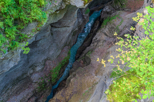 Aerial view from a suspension bridge overlooking a narrow turquoise stream cutting through a deep rocky gorge near Partnachklamm, Garmisch-Partenkirchen, Bavaria.
