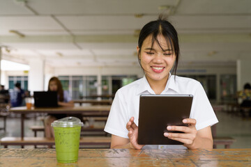 Obraz premium Thai University Student Sitting Alone at Campus Cafe Outdoors Using Tablet Computer