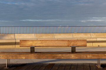 Wooden bench with warm sunset sunlight on a pier under cloudy sky in St Kilda, Melbourne