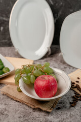 A white ceramic bowl filled with fresh, colorful fruits and vegetables. Healthy eating concept with apple, grapes, orange, and bell pepper.