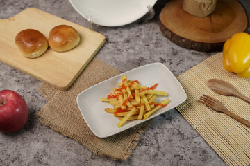 Flat lay of french fries with ketchup, fresh apple, bread rolls, and bell pepper on a grey textured...