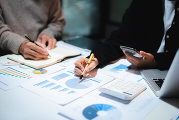 business documents on office table with tablet, smart phone and laptop and two colleagues discussing data