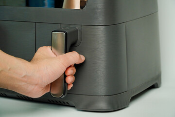 air fryer.man holding is opening the basket of an air fryer in a sunny kitchen