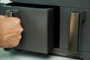 air fryer.man holding is opening the basket of an air fryer in a sunny kitchen