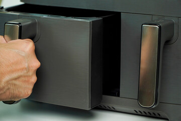 air fryer.man holding is opening the basket of an air fryer in a sunny kitchen