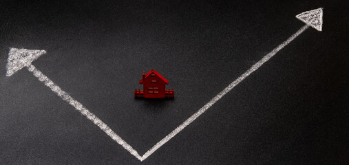Miniature wooden house against the background of financial chart arrows