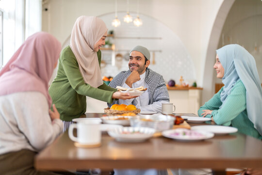 Muslim big family sharing traditional meal together around dining table wearing hijabs and kufi in cultural love, ramadan iftar celebration, eid al-fitr festive, halal meal gathering food culture - Powered by Adobe