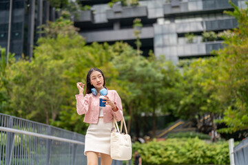 Asian businesswoman stylish with coffee and headphones walking confidently in city, urban...