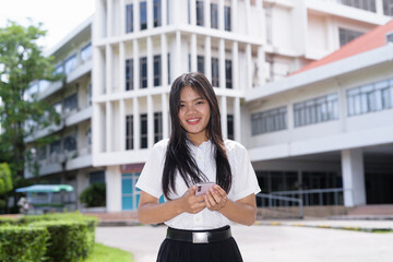 Fototapeta premium Thai Teenager Female Student Standing Outside University Building Using Phone