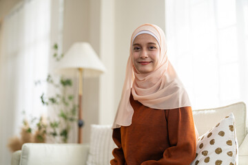 Muslim woman wearing peach hijab smiling peacefully in room at home showing modest calm expression...