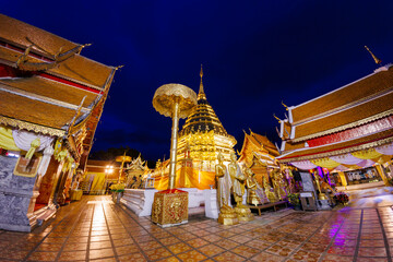 Majestic golden pagoda of Wat Phra That Doi Suthep glows against the night sky, framed by ornate archway, captured with a fisheye lens. Sacred landmark.
