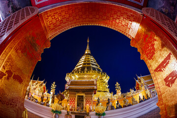 Majestic golden pagoda of Wat Phra That Doi Suthep glows against the night sky, framed by ornate archway, captured with a fisheye lens. Sacred landmark.
