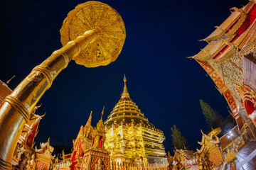 Majestic golden pagoda of Wat Phra That Doi Suthep glows against the night sky, framed by ornate archway, captured with a fisheye lens. Sacred landmark.
