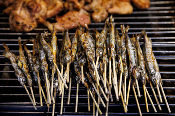 Delicious grilled Shishamo (Japanese smelt or capelin), seasoned with salt and filled with roe, being cooked on a hot barbecue grill. A popular and savory Japanese street food or snack.
