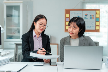 Two asian businesswomen are working together in the office, using a laptop and analyzing financial...