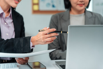 Two businesswomen engaged in a work discussion, pointing at a laptop screen with a pen while...