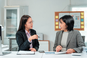 Two young businesswomen analyzing financial data and discussing project strategy during meeting in...
