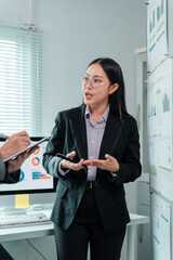 Asian businesswoman wearing suit and glasses is holding a pen and explaining project strategy to...