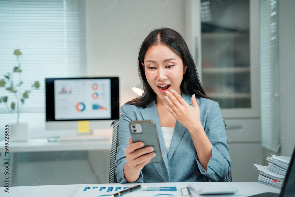 Poster asian businesswoman working with financial documents using smartphone and computer showing surprised