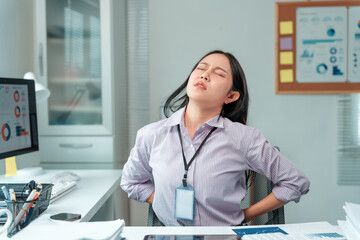 Young businesswoman gripping her lower back, displaying a pained expression while enduring backache...