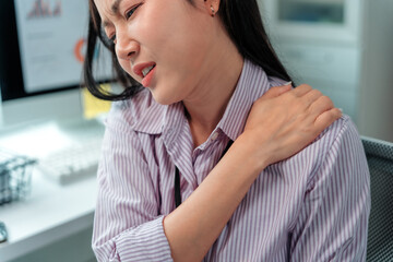 Young businesswoman massaging her shoulder, dealing with neck and shoulder pain after long hours...