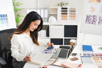 Interior designer working on her project  in studio office holding pen taking notes in a notepad .