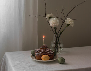 Easter still life - buns, brioche, candle, painted eggs, bouquet of flowers on the table