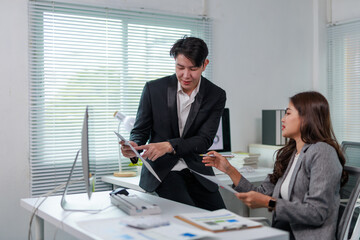 Two Asian businesspeople collaborating in a modern office, analyzing financial statistics on a...