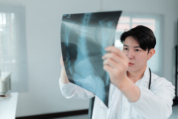 Young practitioner wearing lab coat and stethoscope is carefully holding and looking at a radiography in a medical office, illuminated by natural light