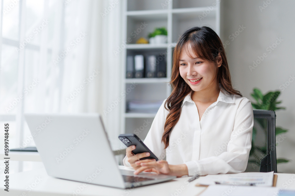 Poster smiling businesswoman using laptop and smartphone while working in modern office, managing her busin