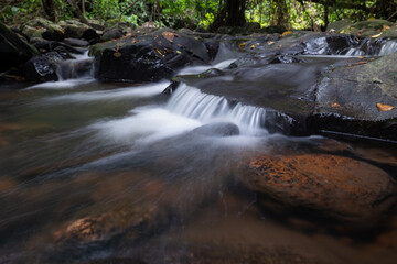 A slow-shutter image capturing silky water cascading over dark stones in the tranquil forest of Jedkot Waterfall, Saraburi, Thailand, on July 20, 2025.