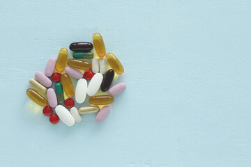 Flat lay with copy space of assorted supplement pills and capsules on a light blue wooden backdrop. Healthy vitamin concept.