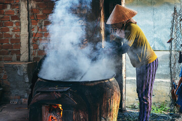 Vietnamese woman in traditional straw hat works in reed dyeing workshop for production of woven...