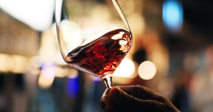 Hand, person and swirl red wine for taste testing, quality control and sensory ritual in glass. Customer, inspection and alcohol for aroma, balance flavor and brewery closeup for event with bokeh