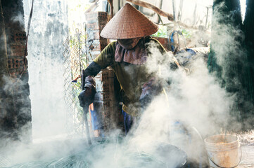 Vietnamese female worker in straw hat works in reed dyeing workshop at wicker mat factory in Vietnam