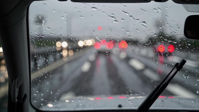 View through a rainy car windshield with water droplets and blurred traffic lights on wet road. Concept of rainy weather and urban driving mood


