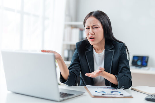 Young businesswoman feeling frustrated while looking at her laptop, gesturing expressively in the office, showcasing the stress and challenges of her work environment
