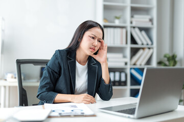 Asian businesswoman suffering from headache and touching her head while using laptop computer at...