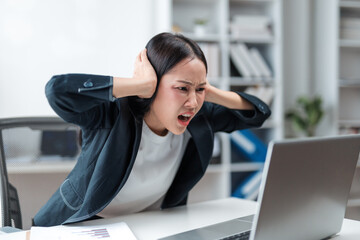Young Asian manager experiencing a headache while covering ears with hands, overwhelmed by the loud...