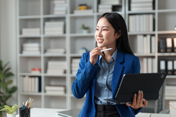 Young Asian businesswoman holding a tablet and stylus pen, contemplating new project ideas in a...